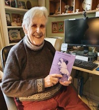 a woman sitting in front of a computer holding a book