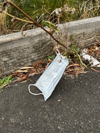 a medical mask lying on the ground next to a fence