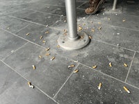 a man is standing next to a metal pole with cigarette ashes on it