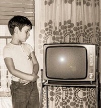 a black and white photo of a boy standing in front of a television