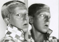 a black and white photo of a young man looking into a mirror