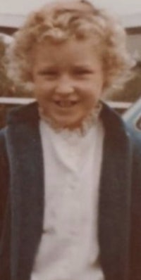 a young girl in a blue jacket standing next to a car